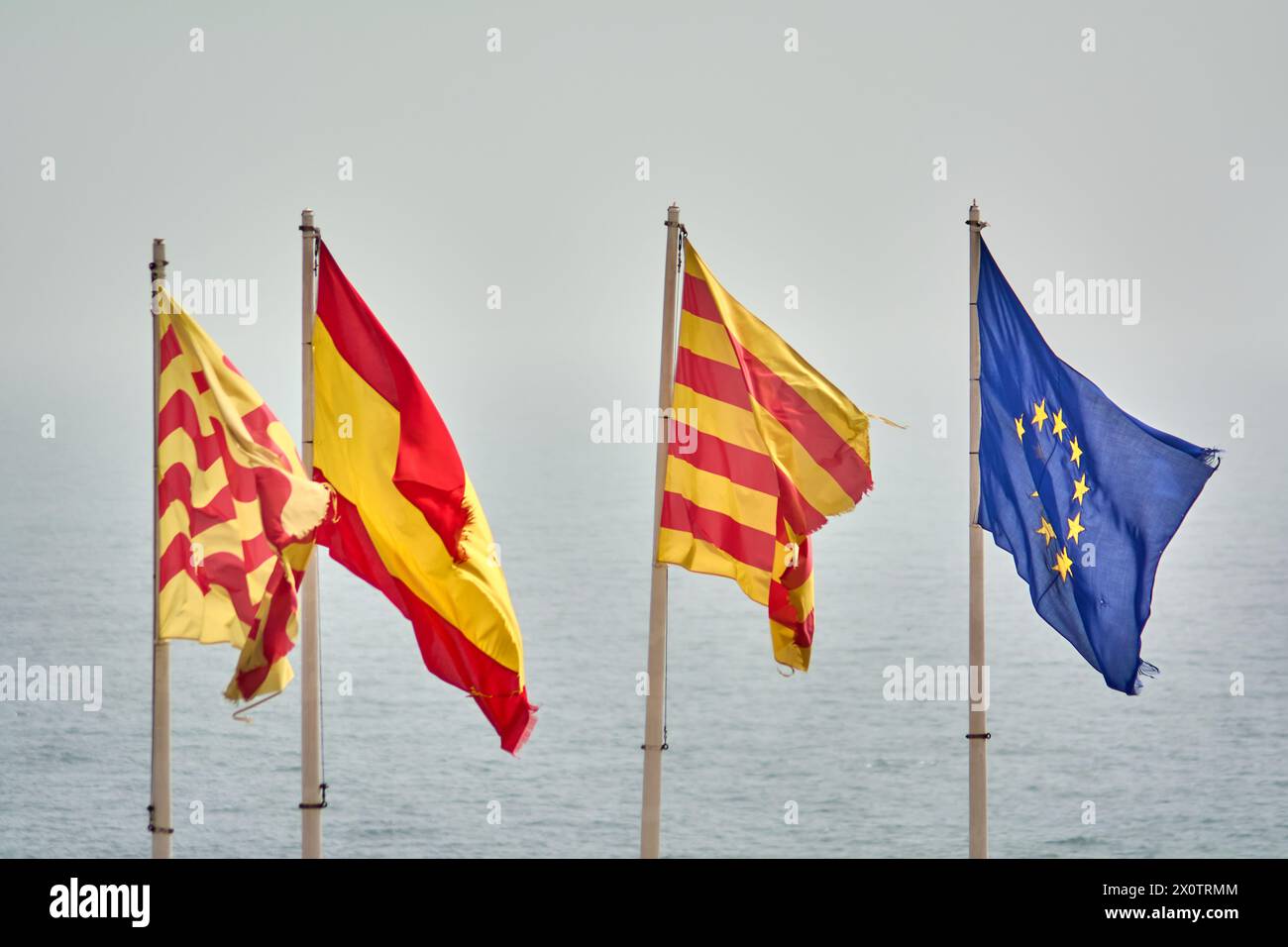 Vier repräsentative Flaggen fliegen zusammen mit dem Meer im Hintergrund und erinnern an die Einheit und kulturelle Vielfalt Europas und seiner Regionen. Stockfoto