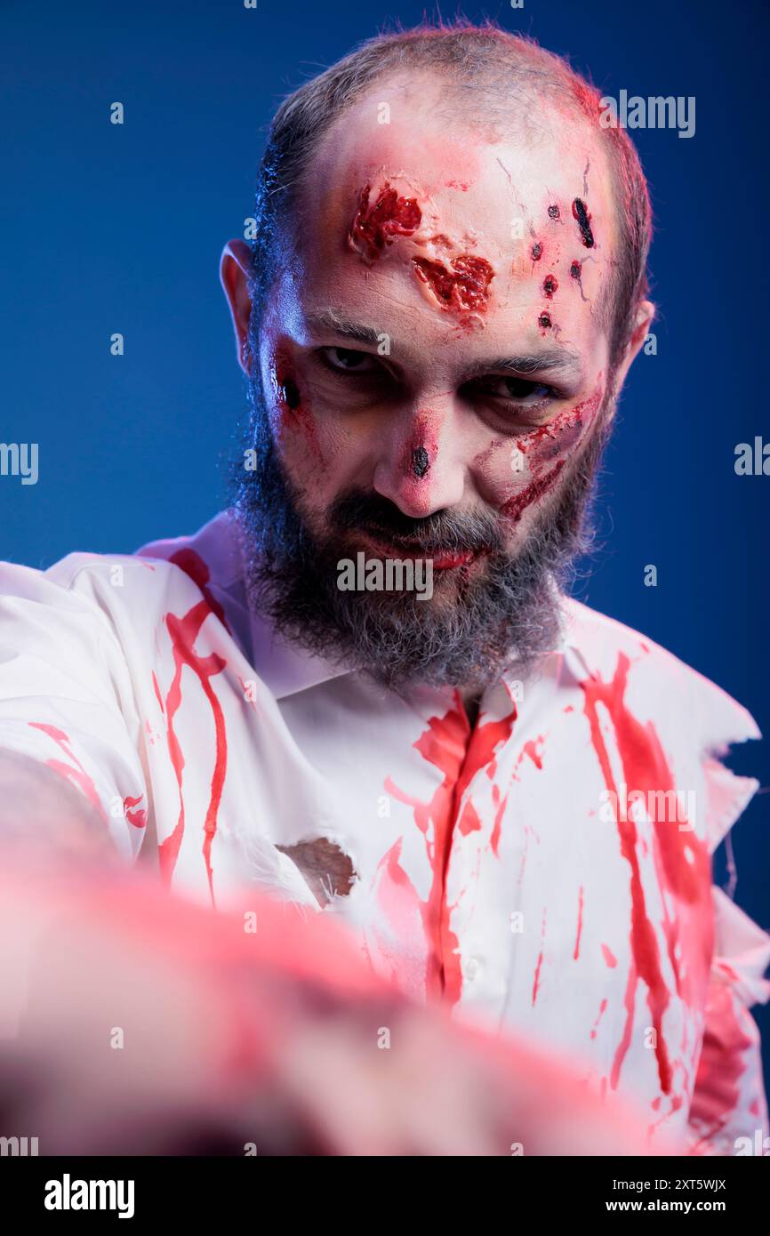 Porträt eines Mannes, der als gefährlicher, finsterer Zombie verkleidet ist, der für halloween-Events mit Blut bedeckt ist. Eine Person mit Gore Make-up, die sich als untote Kreatur mit Narben, Studiohintergrund ausgibt Stockfoto