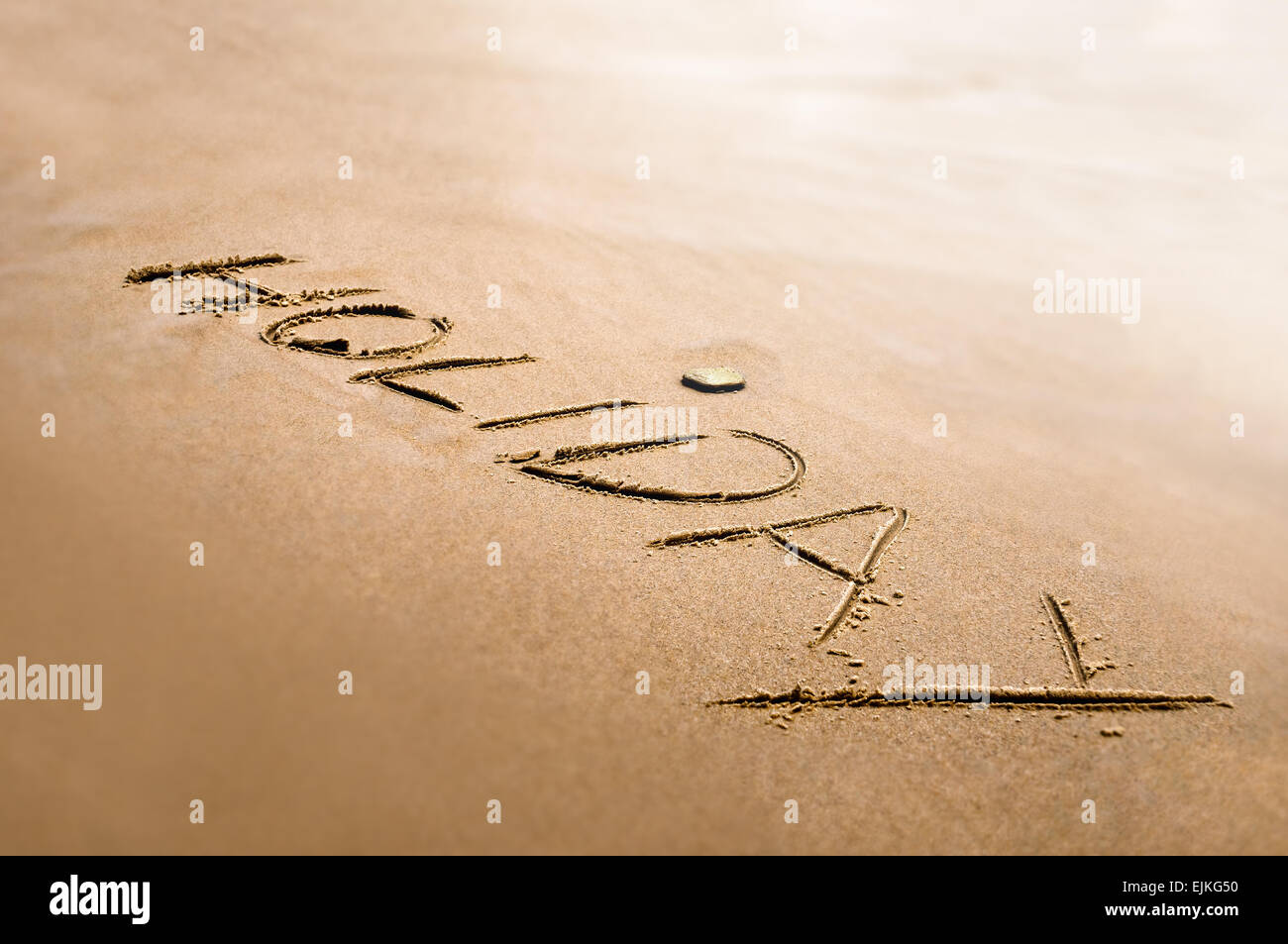 Urlaub-Wort geschrieben auf dem hellen Sand zurück Lichteffekt Stockfoto