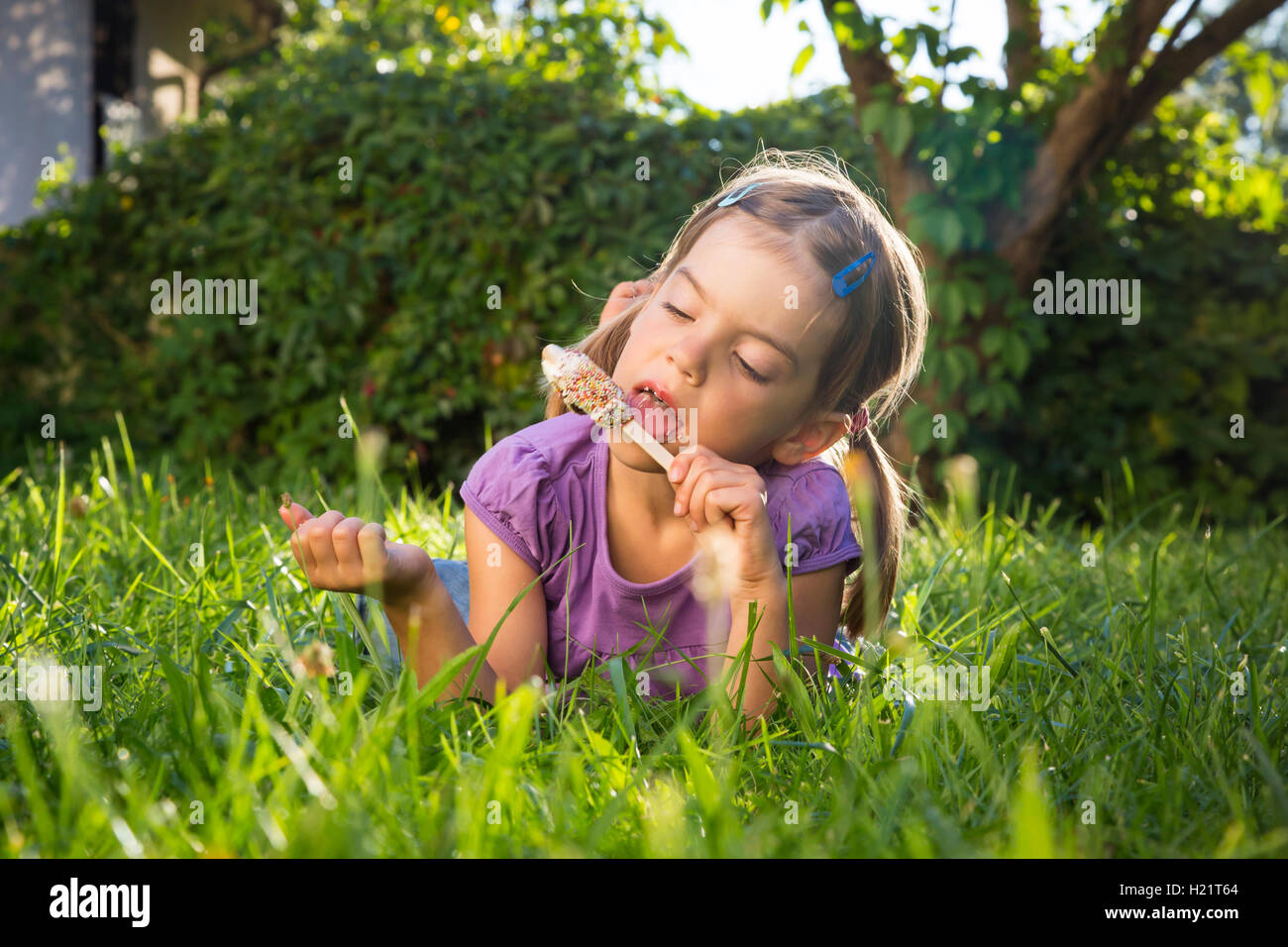 Kleines Mädchen auf Wiese essen Eis am Stiel Stockfoto