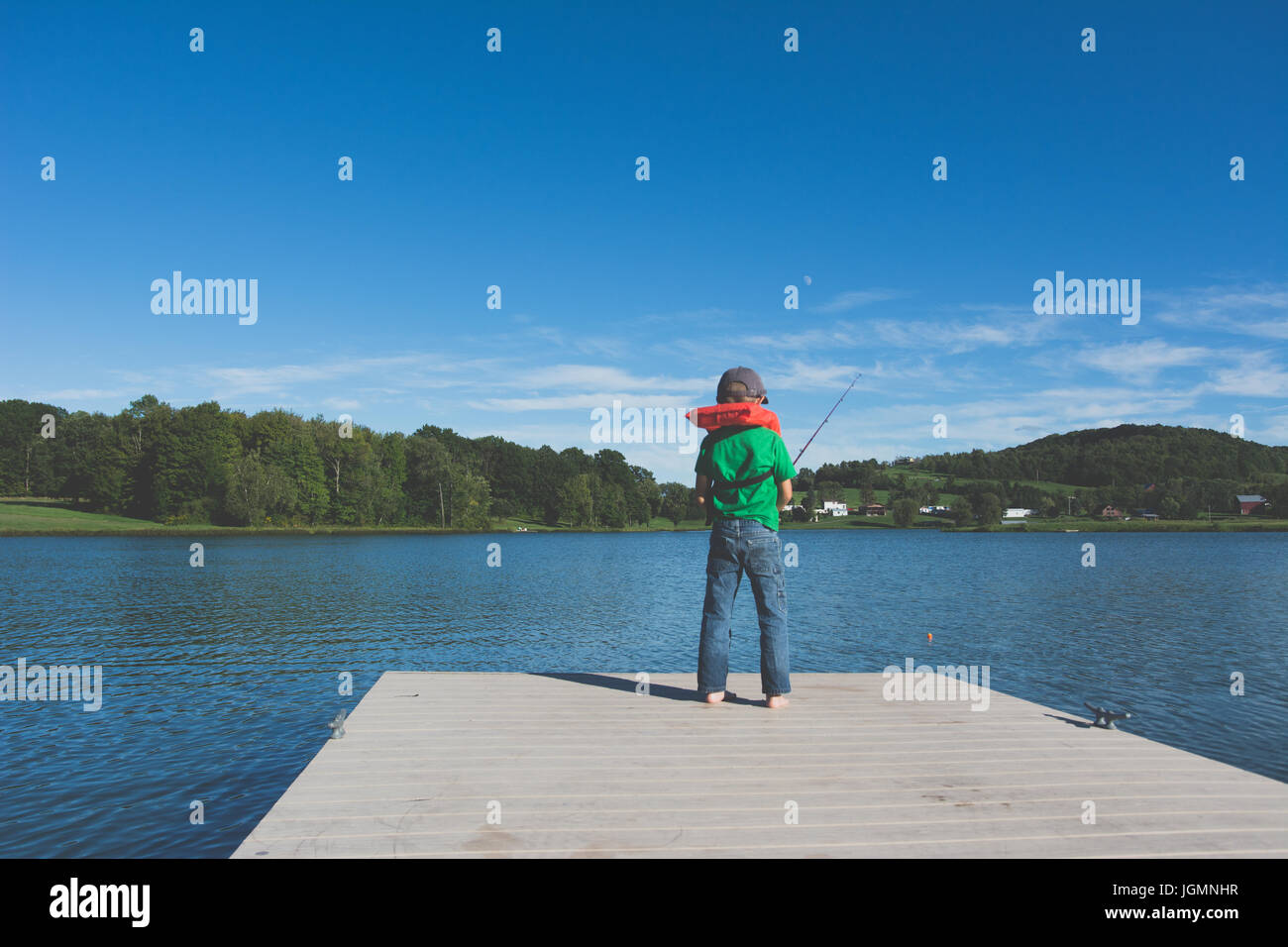 Ein Kind, Angeln an einem Dock an einem Teich in einer ländlichen Gegend. Stockfoto