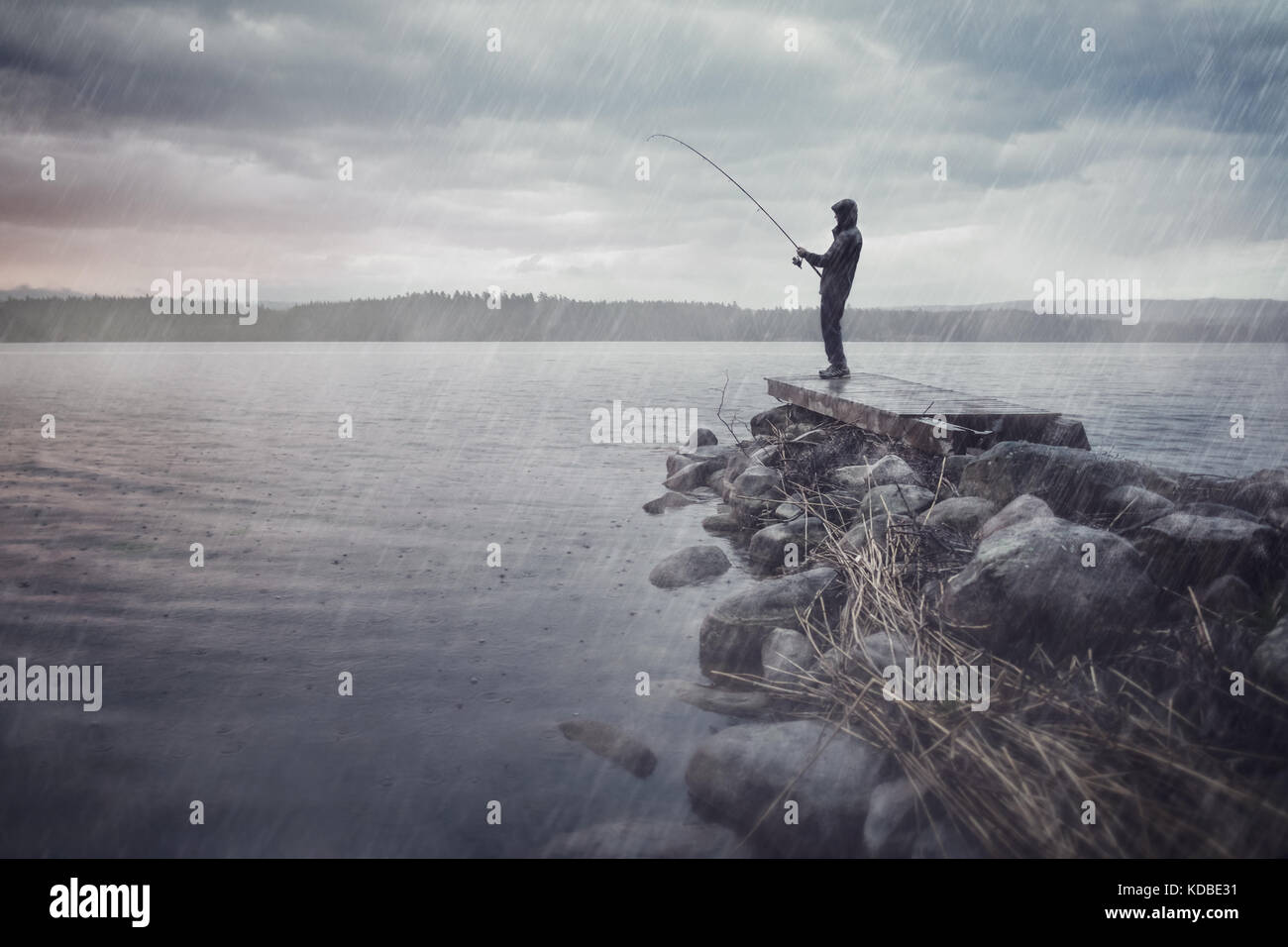 Mann, der an einem See Angeln im Regen Stockfoto