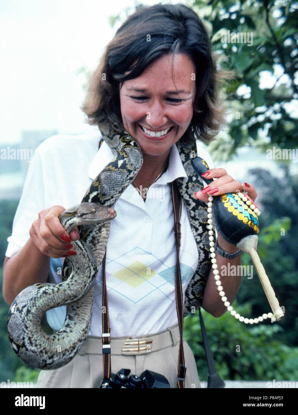 Eine weibliche Touristen ermöglicht eine Tigerpython Schlange um den Hals drapiert werden, während sie für ein Souvenir Foto in Singapur Posen. Das Reptil ist die zahmen Haustier von einem lokalen Schlangenbeschwörer, der sein Leben unterhaltsam macht Besucher zu dieser Insel Nation in Südostasien. Obwohl diese grosse Schlange ausgebildet worden, nicht aggressiv zu sein hat, die CONSTRICTOR kann seinen langen Körper um Beute wickeln und es zu Tode quetschen. Anderen Schlangenbeschwörern verfügen über giftschlangen wie Kobras und Vipern aber die Reißzähne oder Drüsen, die Ihre giftige Gift produzieren, die Reptilien entfernt wurde. Stockfoto