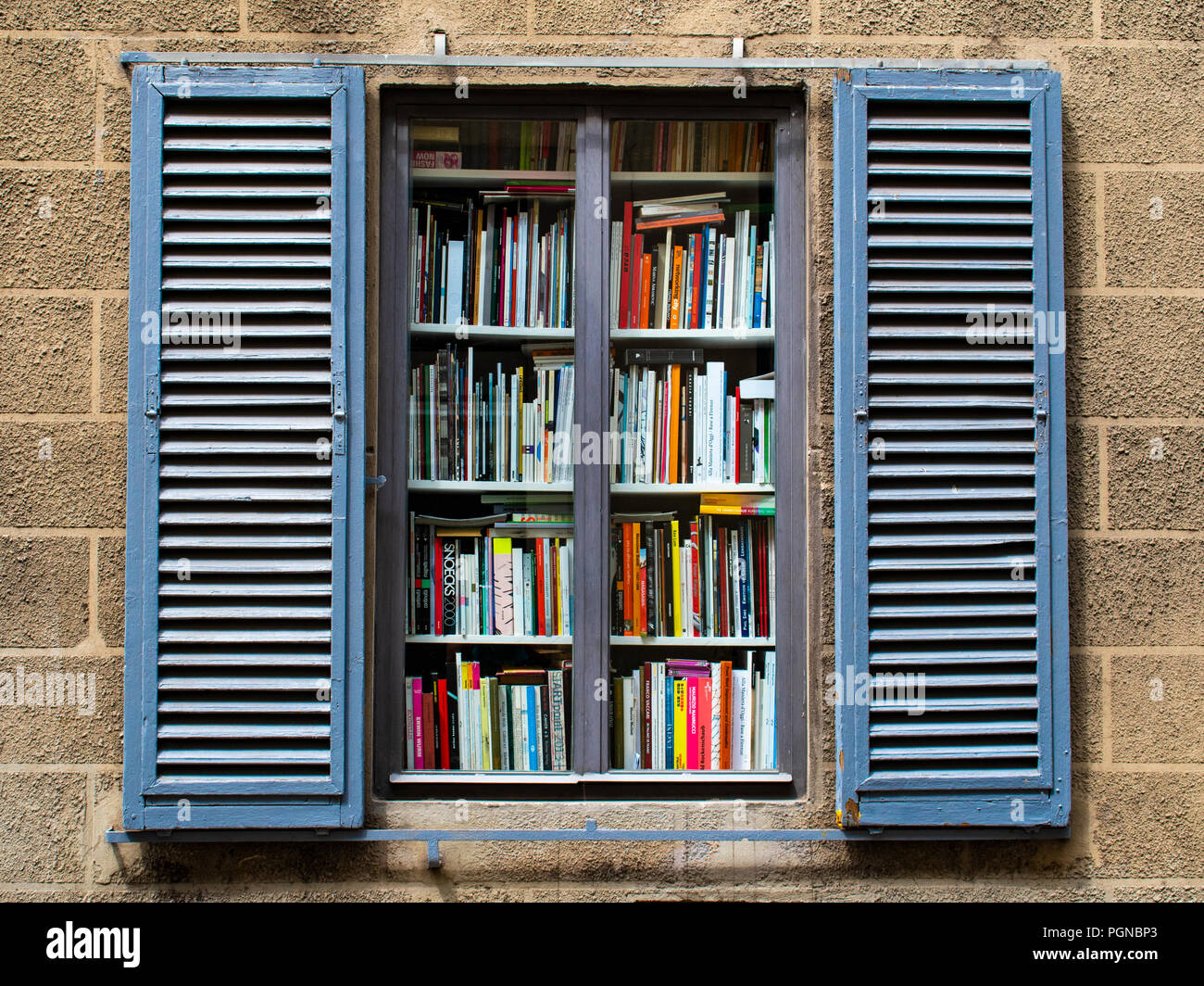 Ein offenes Fenster an der Wand mit einem Bücherregal voller bunter Bücher Stockfoto