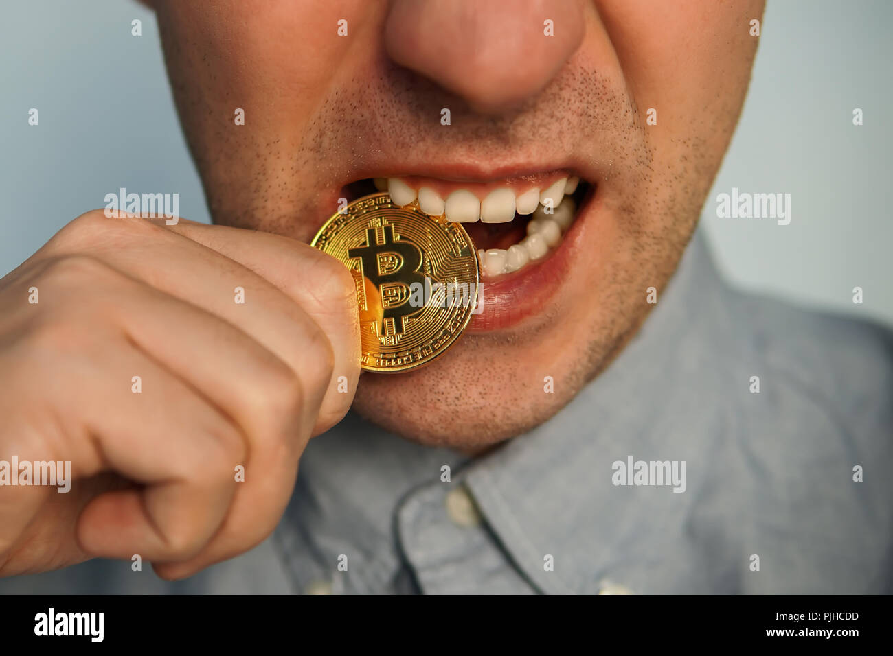 Ein Geschäftsmann versucht, eine goldene bitcoin Zähne. Das Böse Grinsen. Stockfoto