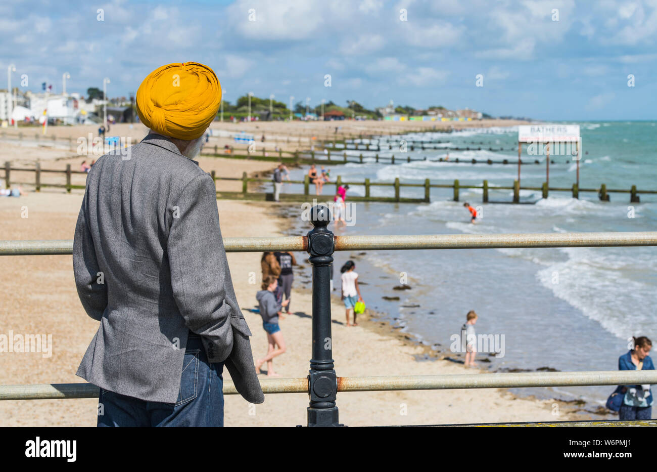 Mann mit dem Turban der Sikhs, stehend auf einem Pier an einem Strand und Meer im Sommer in Littlehampton, West Sussex, England, UK. Stockfoto