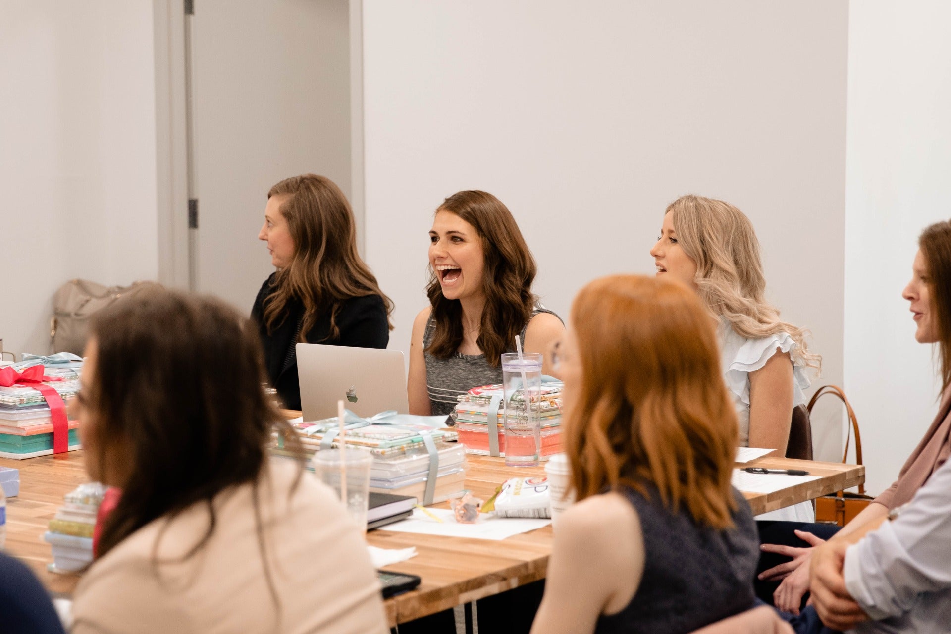 A group of women engaged in discussion around a table in a professional meeting room setting.