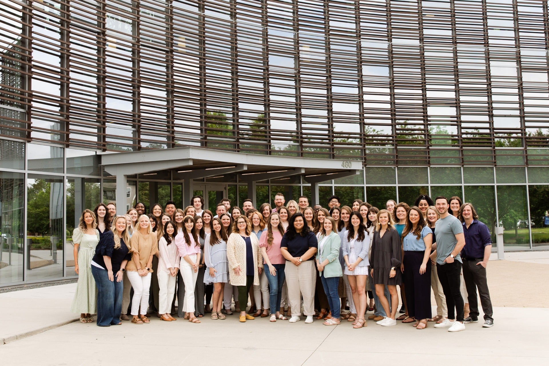 A diverse group of individuals stands together in front of a large building, smiling and engaged in conversation.