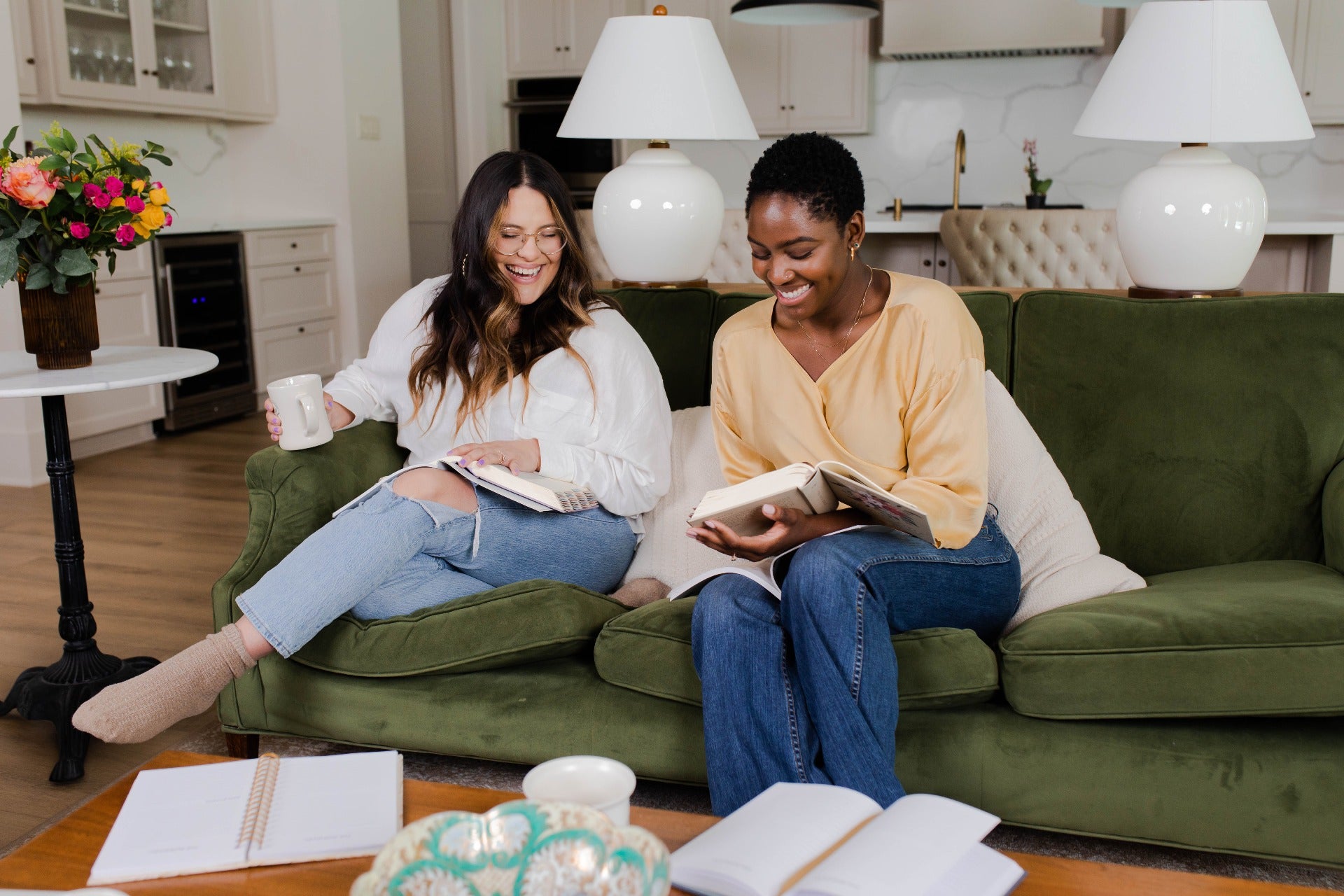 2 women in a sofa happily discussing with books in their hands