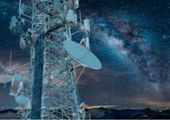 5G communications tower in the left foreground with the Milky Way appearing in the night sky behind it.