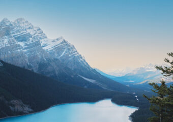 Landscape photo of lake in a mountain range, with a pink and blue daylight sky in the background.