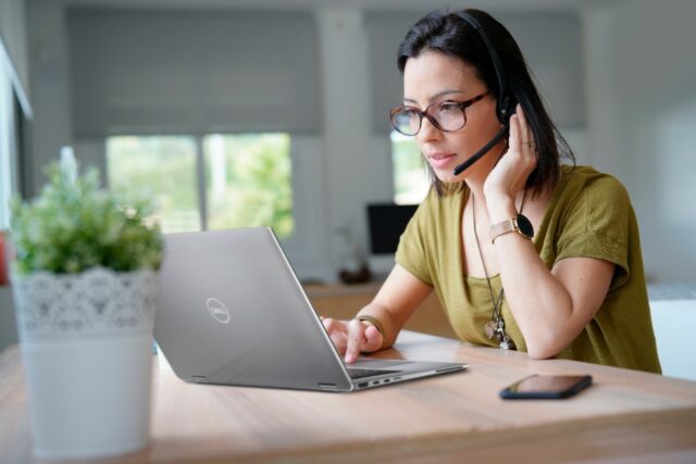 Young woman with glasses and a headset takes part in a meeting remotely using her Dell Latitude 9510 laptop.