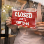 Woman putting red sign with words "Closed Due To Covid-19" onto